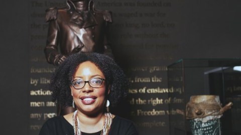Headshot of Joanne Hyppolite standing in front of a tall sculpture on a dark wall background